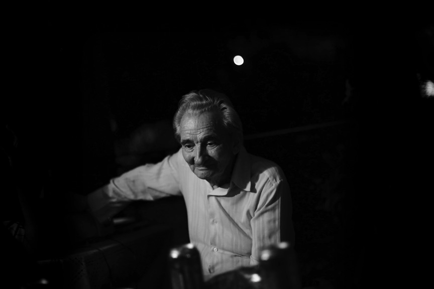 Photographie en noir et blanc de Licu, un homme de 92 ans regardant dans le vide. Il est assis sur une chaise.